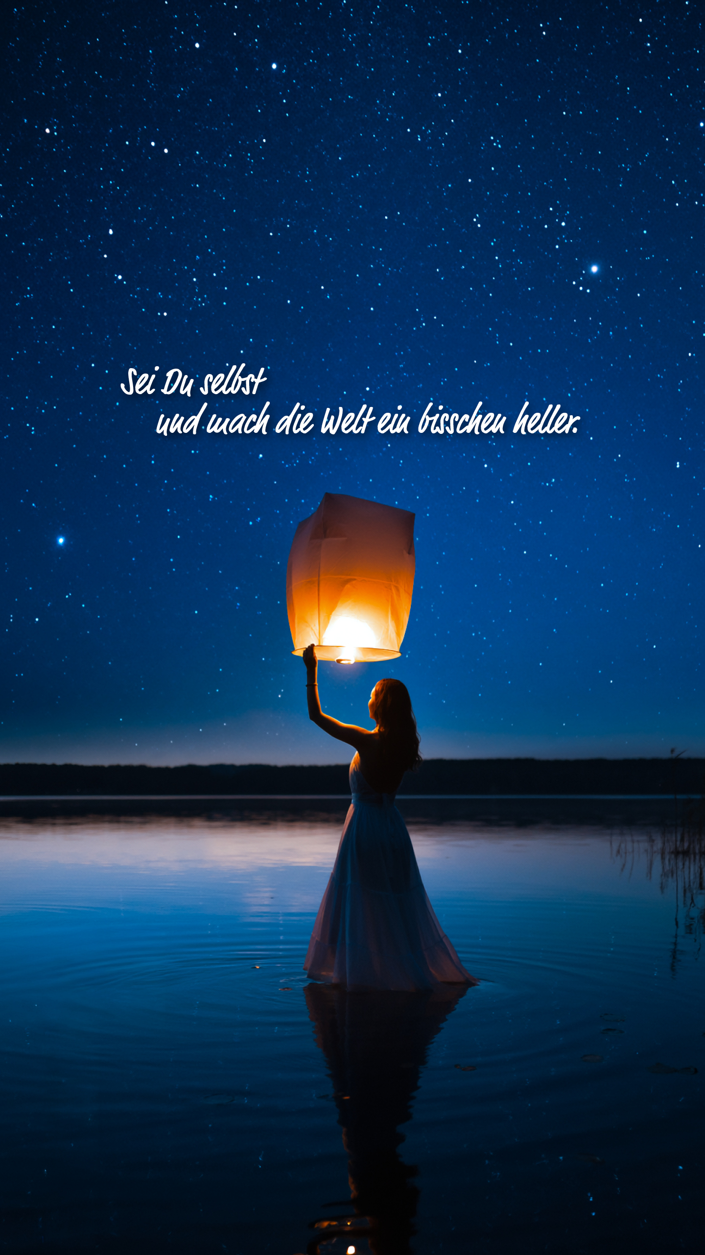Eine Person steht in einem See und hält eine leuchtende Himmelslaterne unter einem Sternenhimmel. Text: Sei Du selbst und mach die Welt ein bisschen heller.